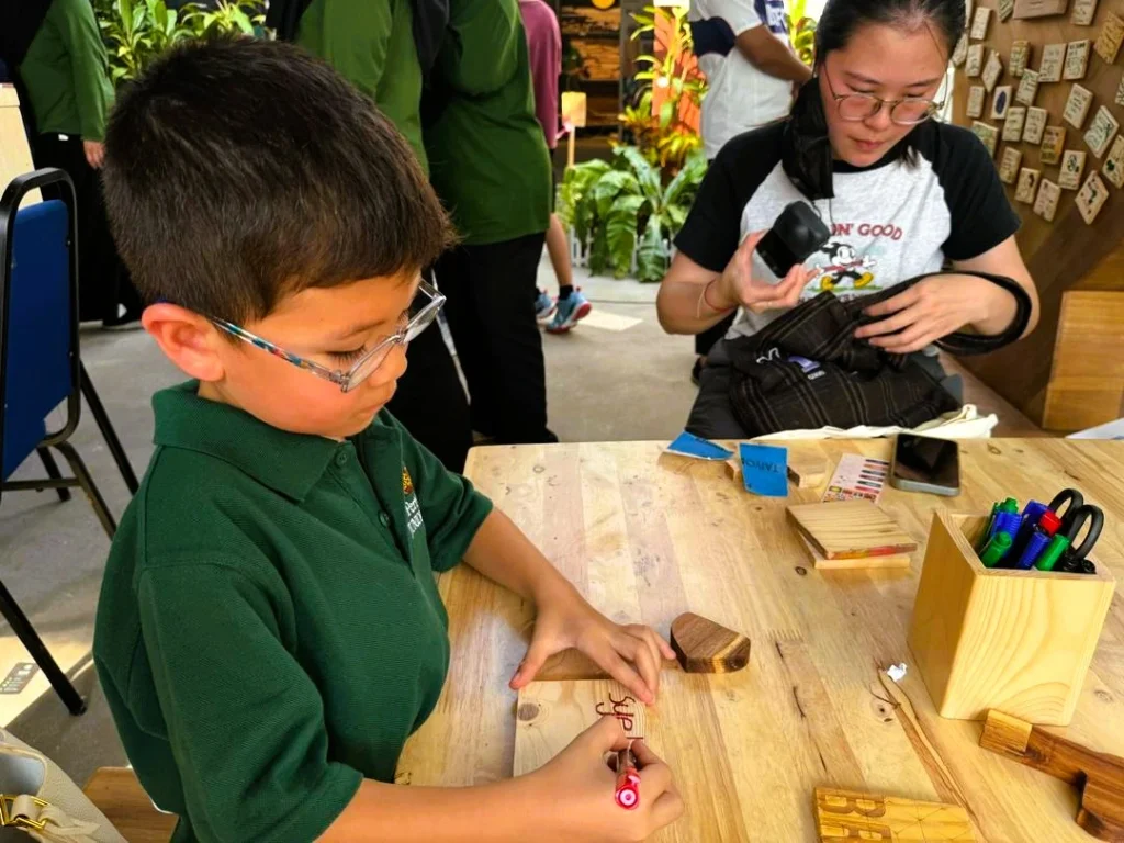 Young participant taking part in a hands-on woodworking activity at Merdekapenter 2026