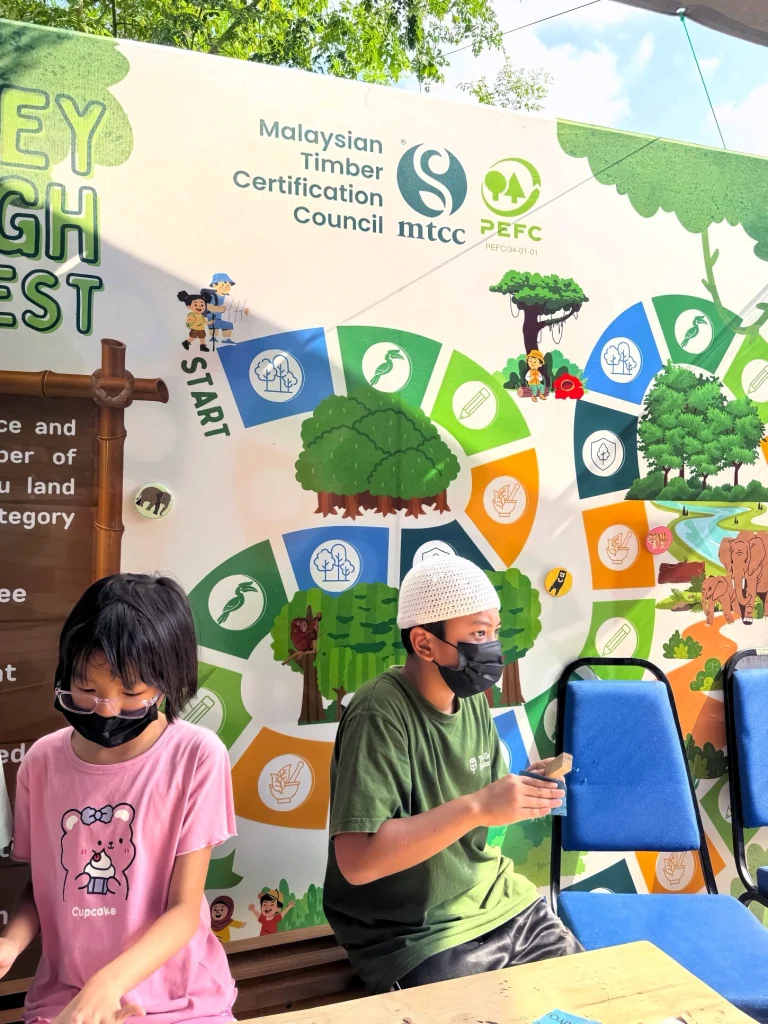 Children participating in sustainability activities at Merdekapenter 2026 alongside the Malaysian Timber Certification Council display